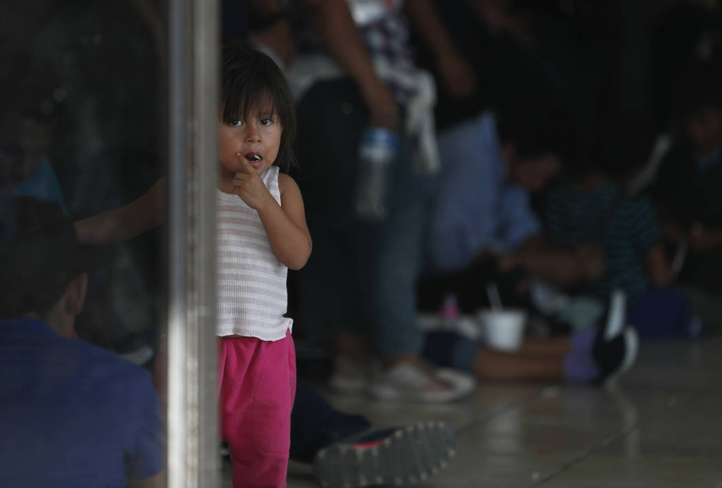 A migrant child looks at the camera while her parents wait at an immigration center on the Inte ...