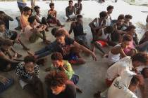 Rescued migrants sit on a coast some 100 kilometers (60 miles) east of Tripoli, Libya, Thursday ...