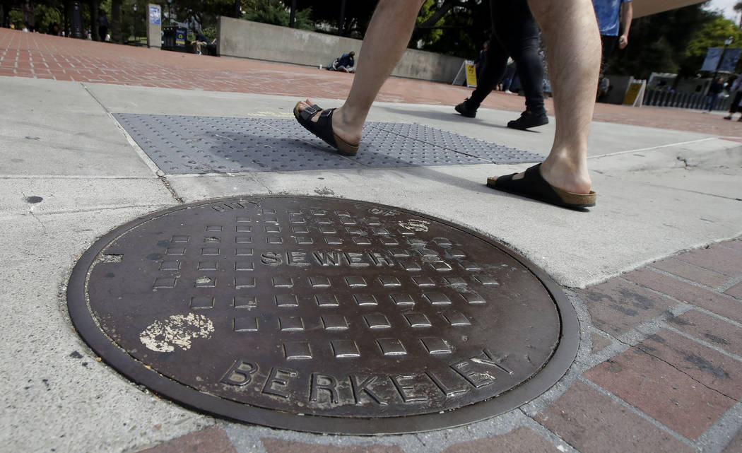 Pedestrians walk past a manhole cover for a sewer in Berkeley, Calif., Thursday, July 18, 2019. ...