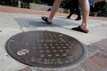Pedestrians walk past a manhole cover for a sewer in Berkeley, Calif., Thursday, July 18, 2019. ...