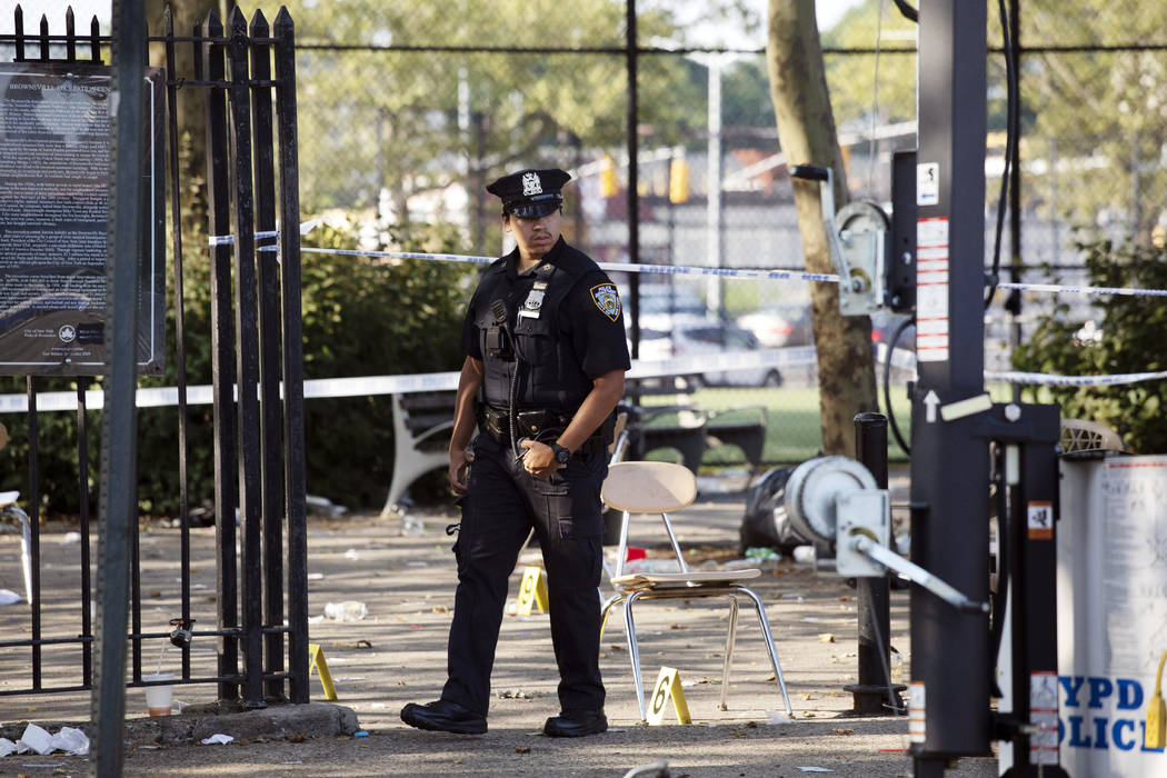 A police officer walks by yellow evidence markers at a playground in the Brownsville neighborho ...