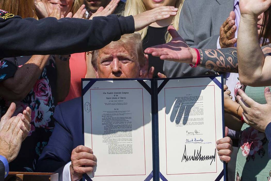 President Donald Trump holds up H.R. 1327, an act ensuring that a victims' compensation fund re ...