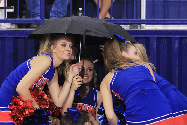 Bishop Gorman cheerleaders huddle under an umbrella during a rain delay before their game ag ...