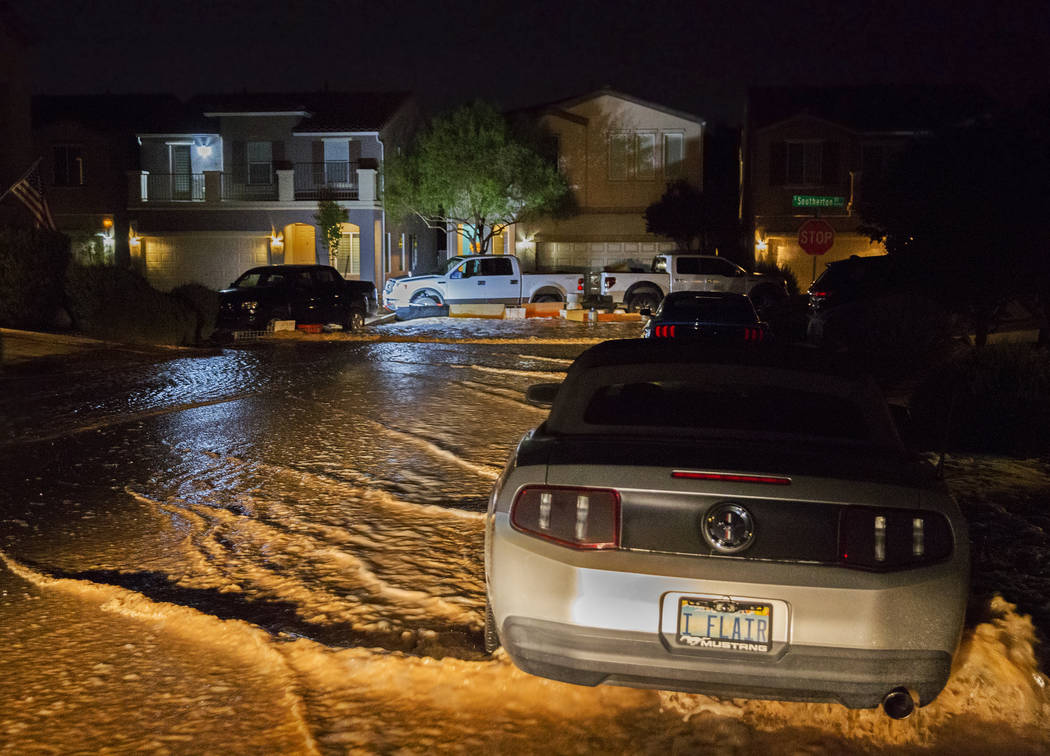 Floodwaters flow past vehicles and homes on West Fitzwilliam Avenue near South Fort Apache Road ...