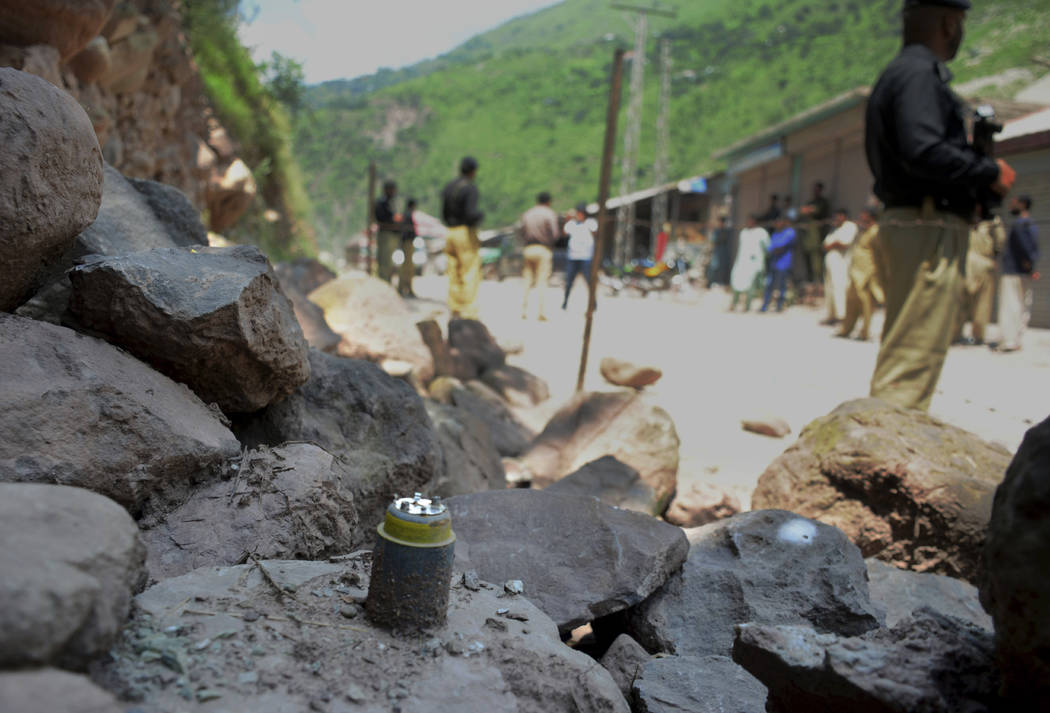 Police officers stand guard next to a munition fired by Indian forces on Nosehri village on the ...