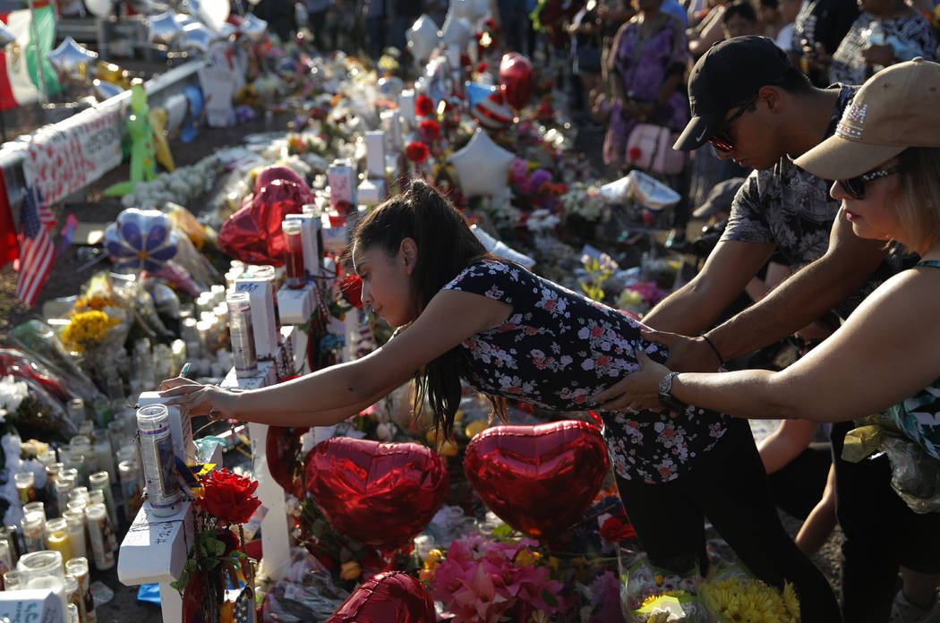 A woman leans over to write a message on a cross at a makeshift memorial at the scene of a mass ...
