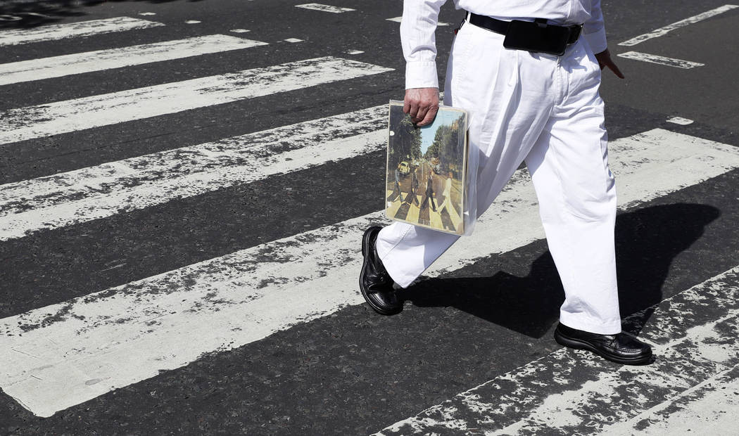 A fan carries a copy of the album 'Abbey Road' as he crosses the Abbey Road zebra crossing on t ...