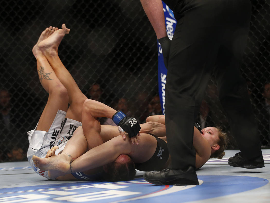 Liz Carmouche, left, taps out as Ronda Rousey pulls an armbar on her during their UFC 157 women ...