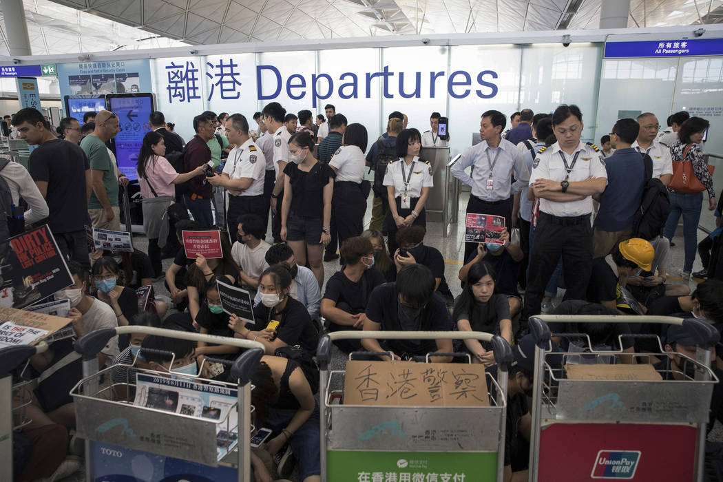 Airport security personnel stand guard as travelers walk past protesters holding a sit-in rally ...