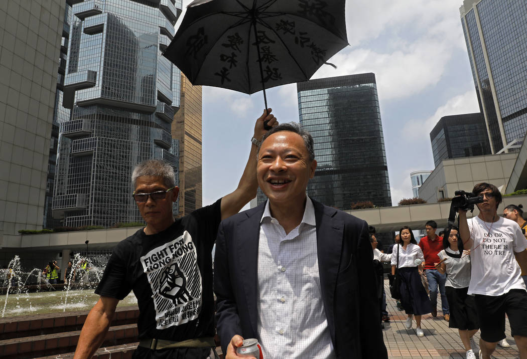 Occupy Central leader Benny Tai, center, is accompanied by a supporter who raises an umbrella a ...