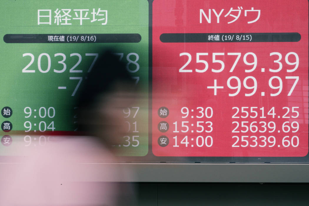 A woman walks past an electronic stock board showing Japan's Nikkei 225 index and NY Dow index ...