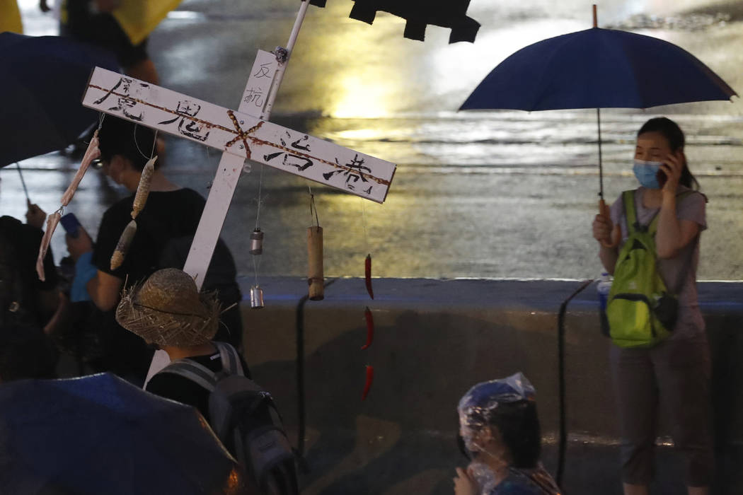 A protester marches with a cross with the words "Devil administers Hong Kong" in the ...