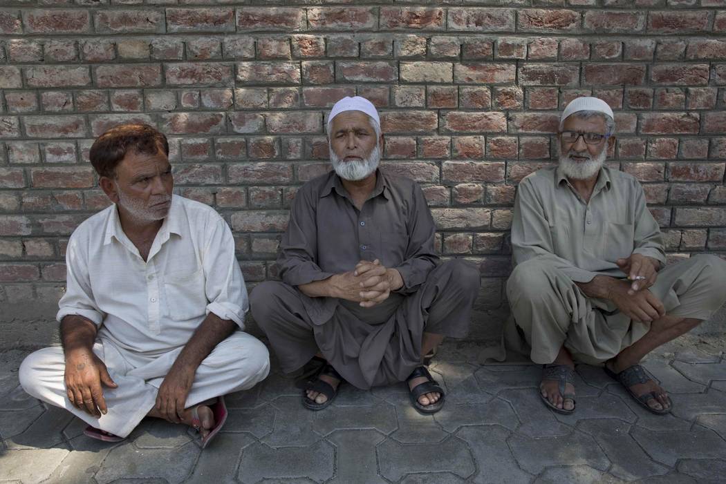 Kashmiri men sit on a footpath outside a police station waiting to hear about their relatives w ...