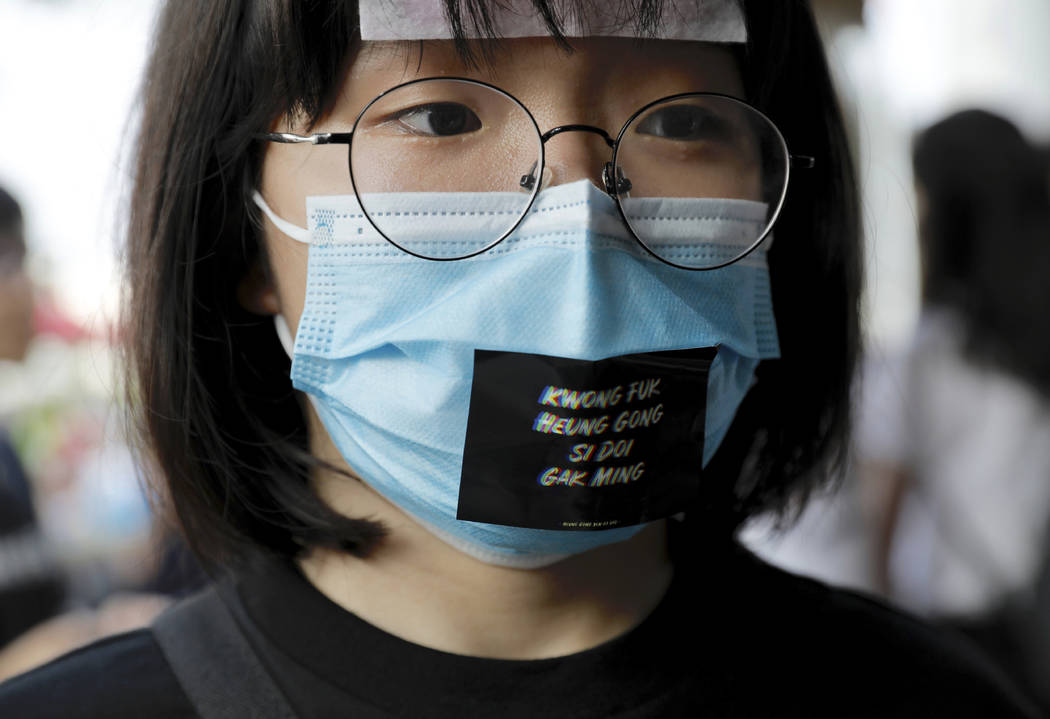 A woman wears a face mask and a sticker reading "Add oil Hong Kong people" during a d ...