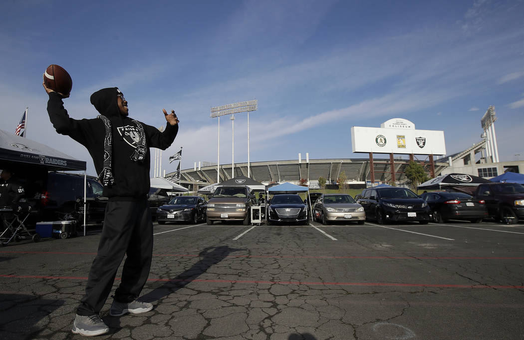 A Raiders fan throws a football as people tailgate outside Oakland Coliseum before an NFL footb ...
