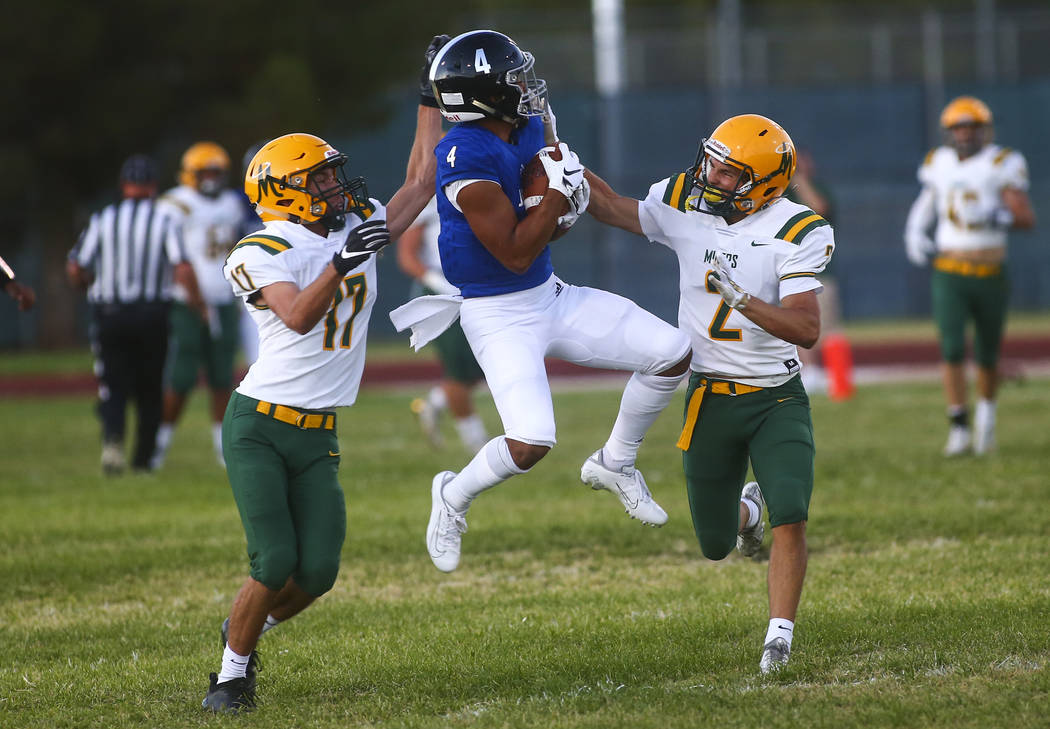 Desert Pines' Branden Thomas (4) catches a pass under pressure from Bishop Manogue's Jaxon Enar ...