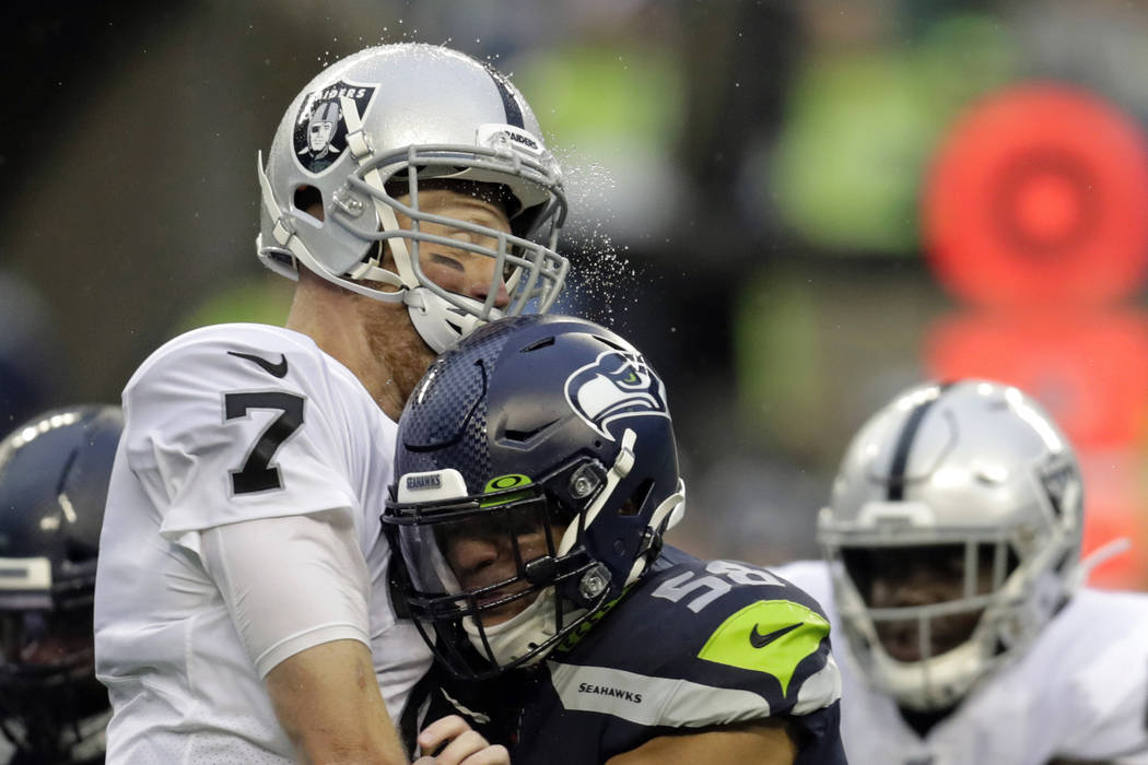 Rain water flies as Oakland Raiders quarterback Mike Glennon, left, is hit by Seattle Seahawks ...