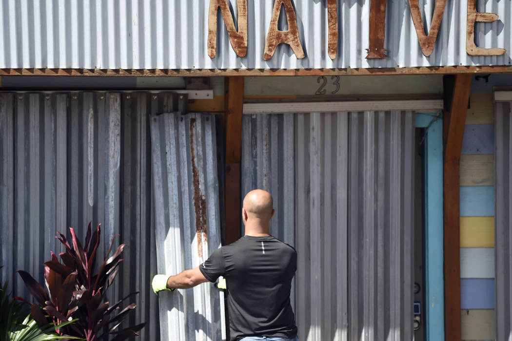 A worker affixes corrugated metal to the front of a business along the main drag in Folly Beach ...