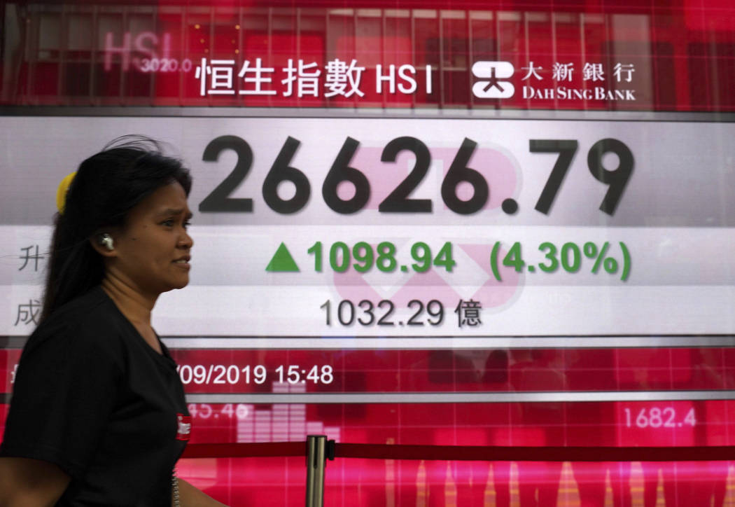 A woman walks past an electronic board showing Hong Kong share index outside a local bank in Ho ...