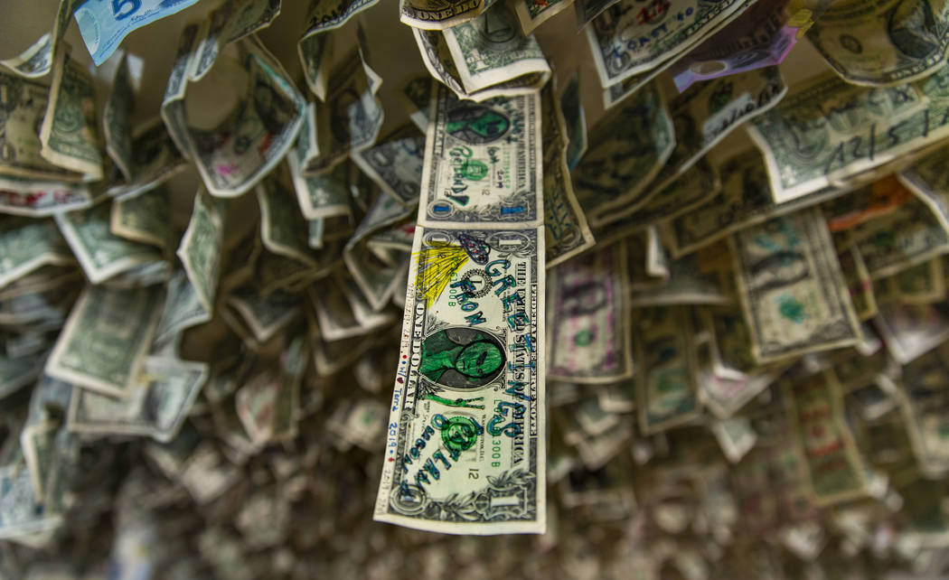 A dollar bill with alien drawing hangs with many other bills above the bar and the restaurant a ...