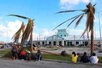 People sit under broken palm trees outside the Leonard M. Thompson International Airport after ...