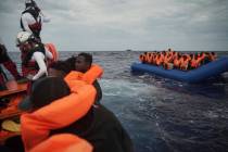 Migrants on a blue rubber boat wait to be rescued some 14 nautical miles from the coast of Liby ...