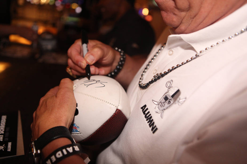 Former Oakland Raider Jay Schroeder signs a football for a fan during a autograph fan signing a ...