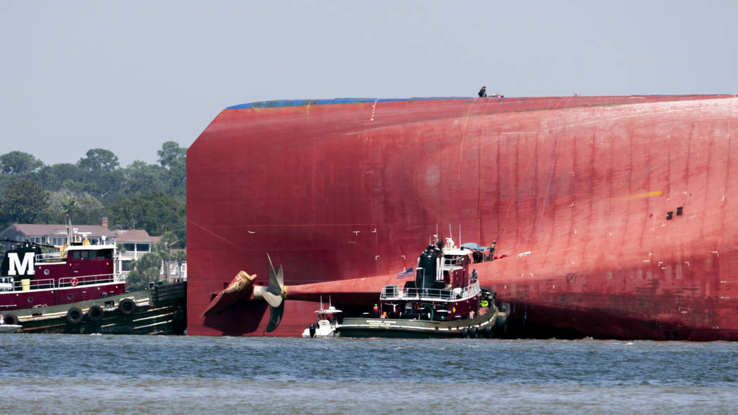 Rescuers work near the stern of the vessel Golden Ray as it lays on its side near the Moran tug ...