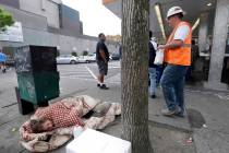 FILE - In this May 24, 2018 file photo, a man sleeps on the sidewalk as people behind line up t ...