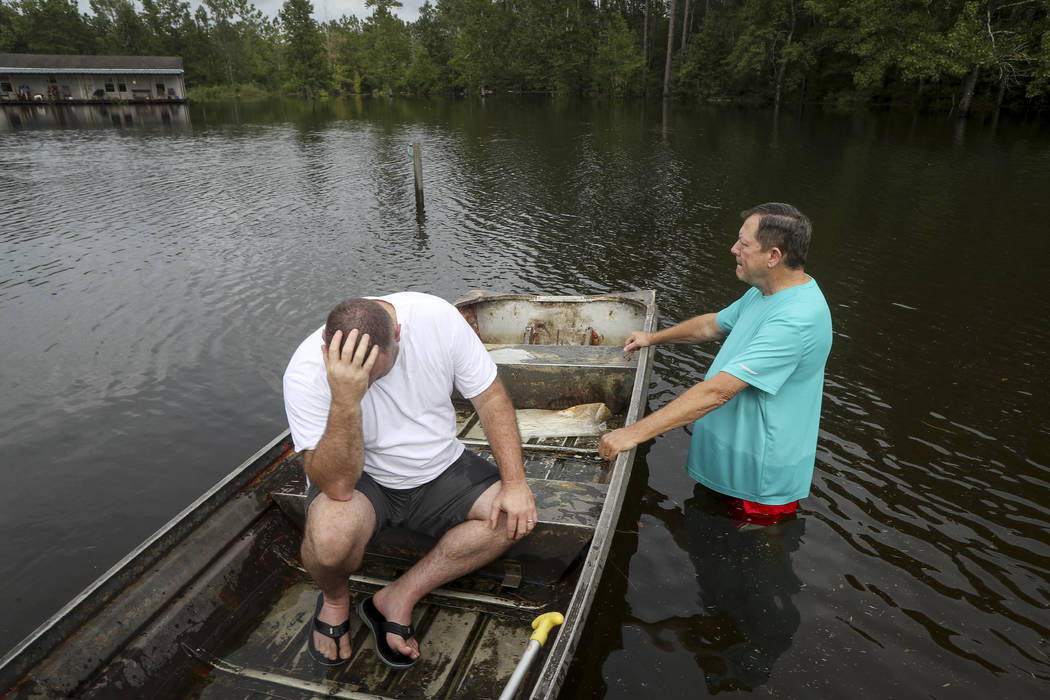 Stephen Gilbert, left, and his father-in-law sit in front of their flooded property on Friday, ...