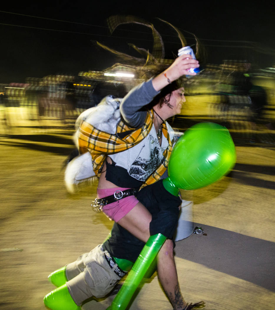 A festivalgoer rides an alien while drinking a beer in the mosh pit at the punk rock stage duri ...