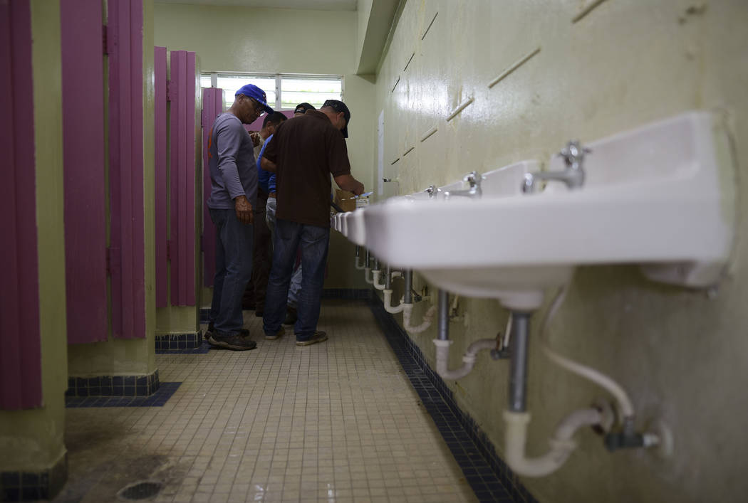 Municipal workers install a shower system in a bathroom at the Ramon Quinones Medina High Schoo ...
