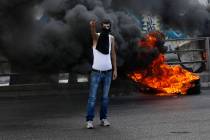 An anti-government protester makes victory sign next to tires that were set on fire to block a ...