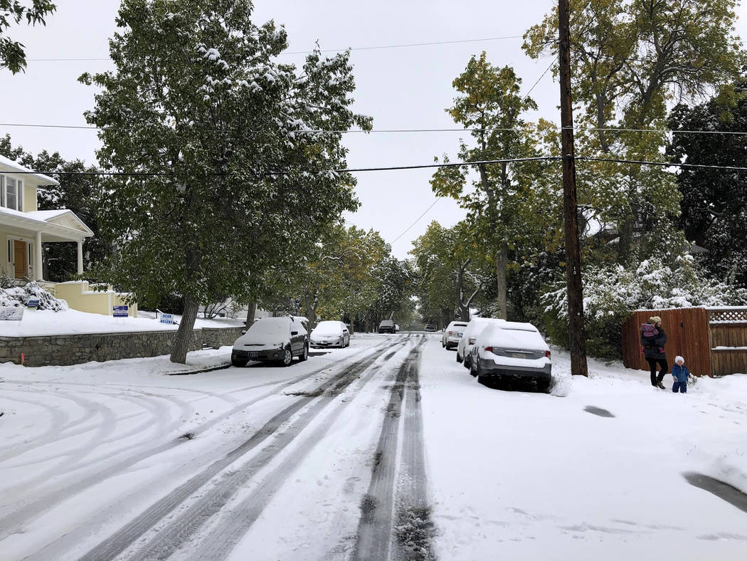 Pedestrians make their way along a snow covered street lined with trees that still have their l ...