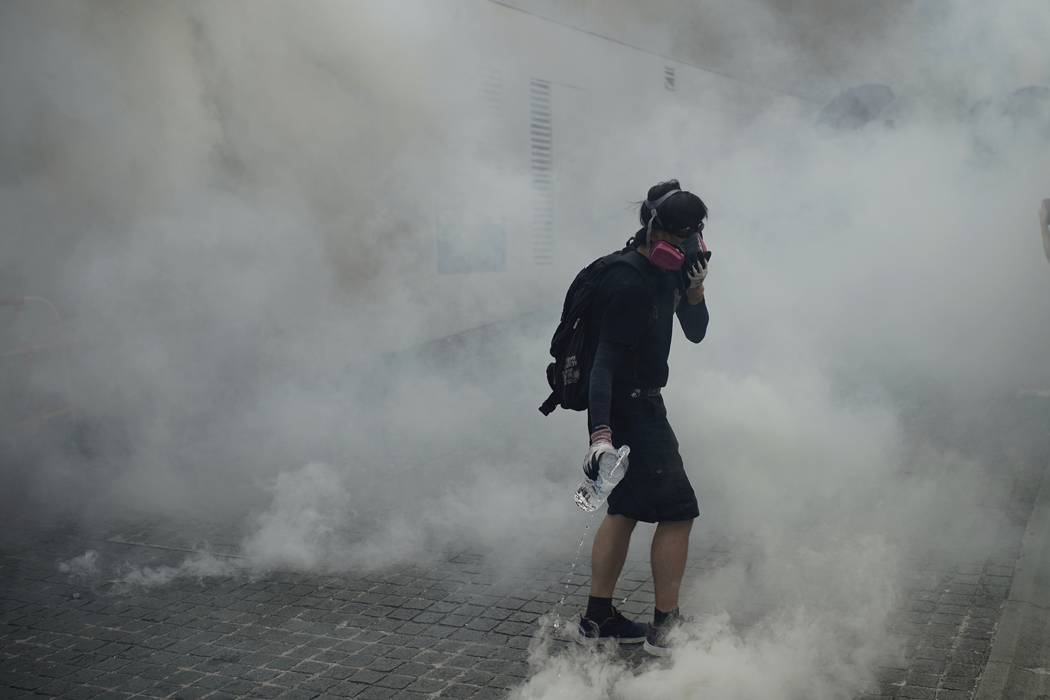 An anti-government protester walks through tear gas smoke during a clash with police at the Won ...