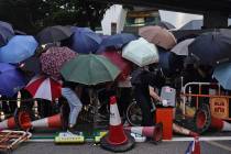 Protesters hide behind umbrellas as they form a barricade to block a road in Hong Kong on Frida ...