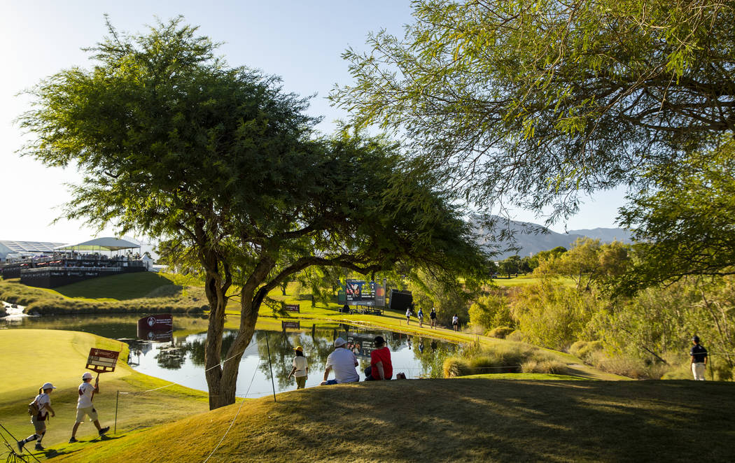 Gallery members take in the day at a water feature alongside the hole 18 fairway during the thi ...
