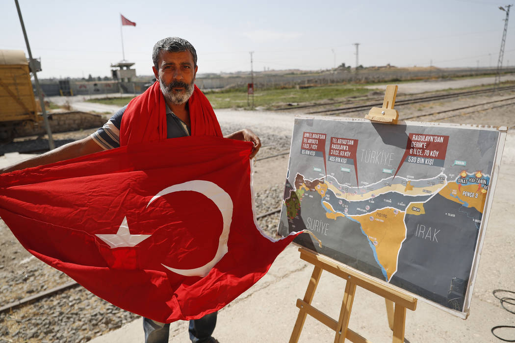 A man holds a Turkish flag as he stands next to a map showing Turkey's suggested operation in S ...