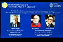 A screen displays the portraits of the laureates of the 2019 Nobel Prize in Physics, with left ...