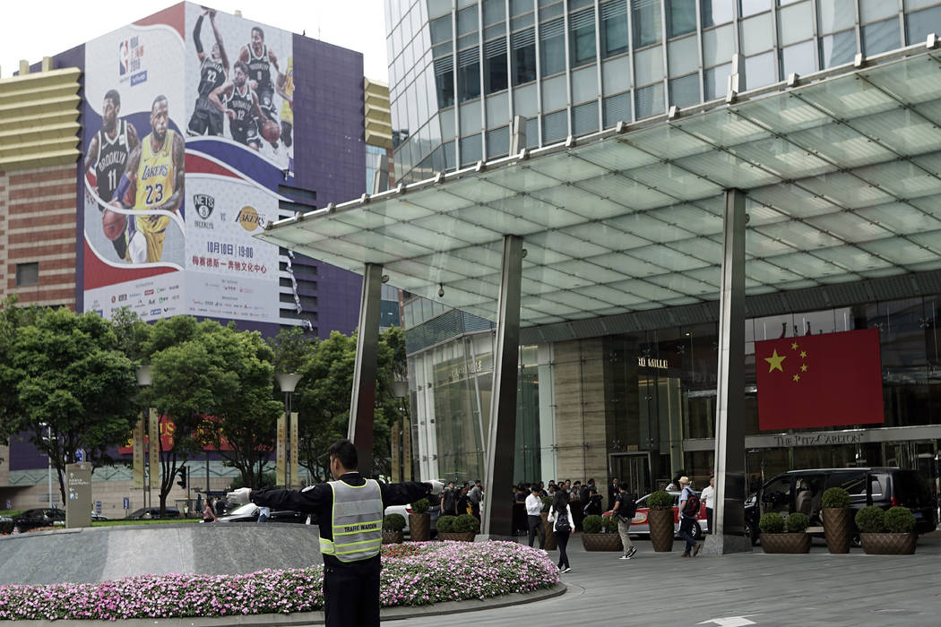 An official directs traffic near a Chinese flag and a billboard advertising an NBA preseason ba ...