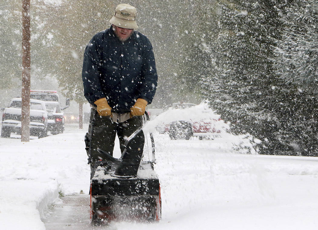 Kevin Hill uses a snow blower to remove snow from his front sidewalk as snow continues to fall ...