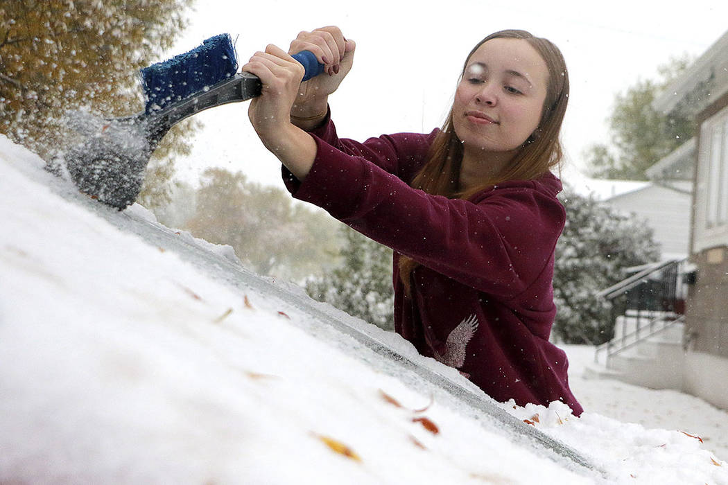 MaKenzie Gregory scrapes ice off her vehicle's front windshield as snow continues to fall in Sc ...
