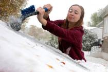 MaKenzie Gregory scrapes ice off her vehicle's front windshield as snow continues to fall in Sc ...
