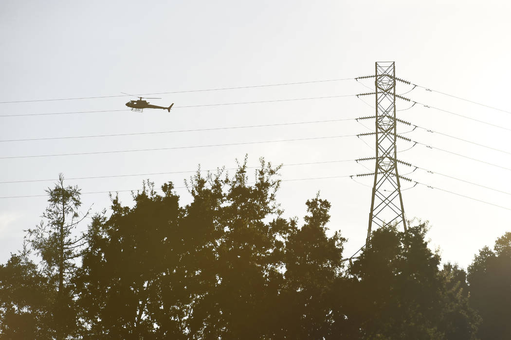 As the sun begins to set a helicopter hovers above large electrical towers while inspecting the ...