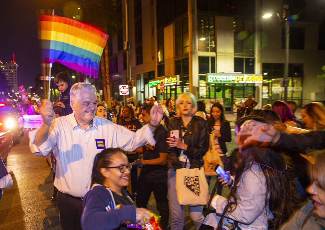 Governor Steve Sisolak waves a flag and helps to pass out Skittles while marching in the Pride ...