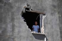 A local resident looks out from a hole on a house that was damaged by a mortar fire from inside ...