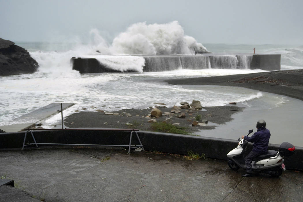 A man on a scooter watches as surging waves hit against the breakwater as Typhoon Hagibis appro ...