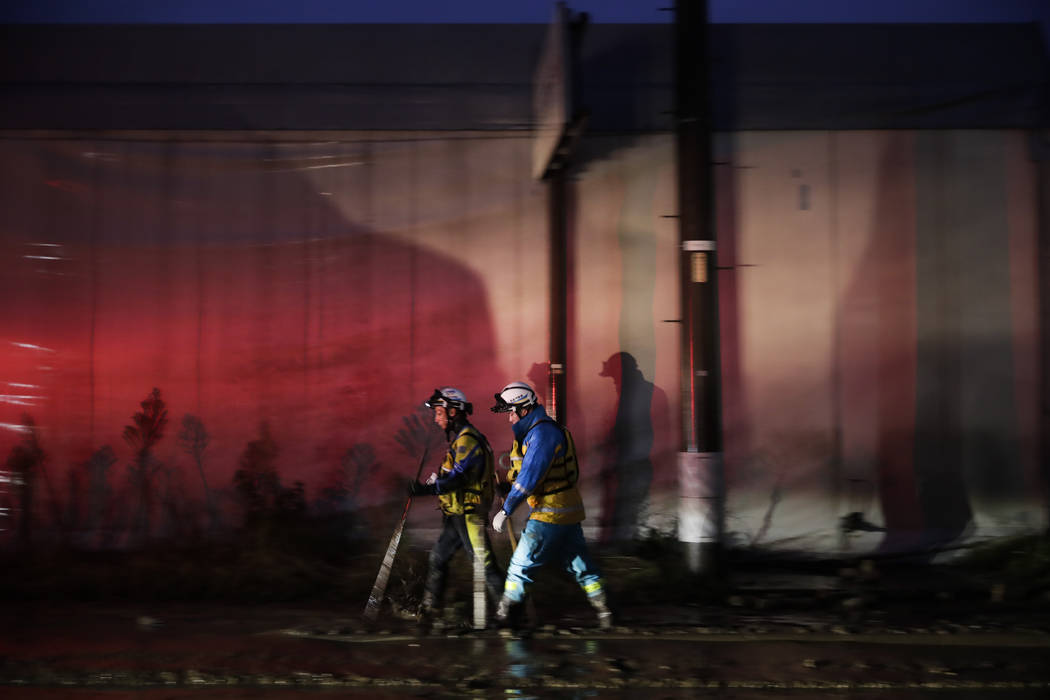 Two search and rescue team members walk along the mud-covered street Monday, Oct. 14, 2019, in ...