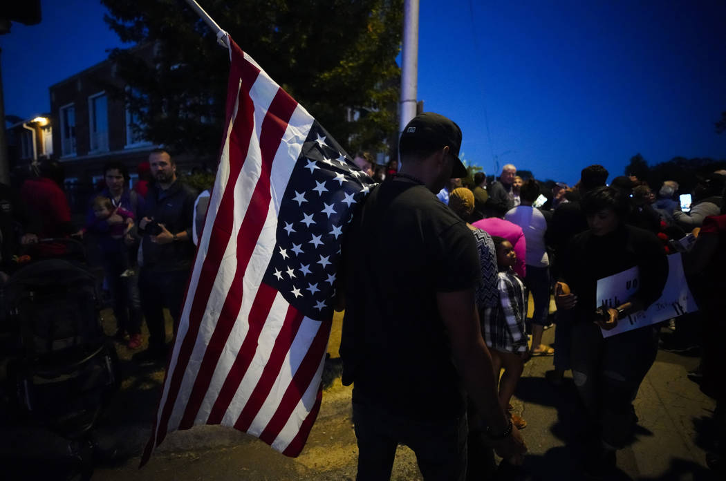 A large crowd of protesters, including a man carrying an upside-down American flag, gather outs ...