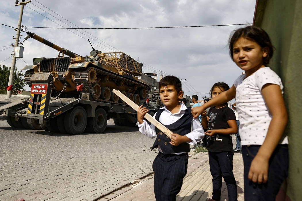 Children watch as army tanks are transported on trucks in the outskirts of the town of Akcakale ...